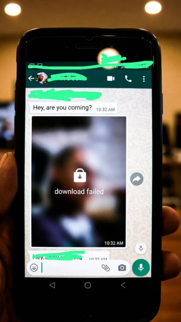 A smartphone screen showing a WhatsApp chat with a blurred image and a failed download icon